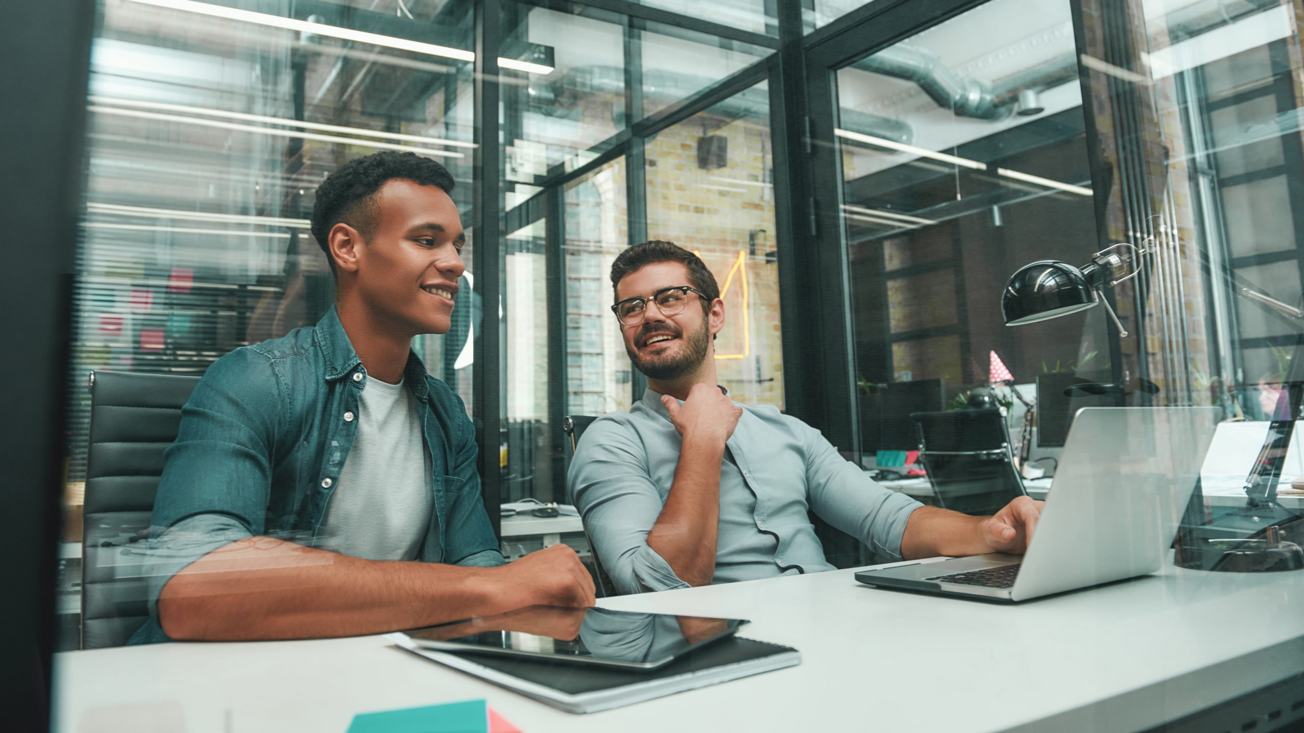 Good communication. Two young and handsome men talking with each other and smiling while working in modern office. Business people. Workplace. Teamwork